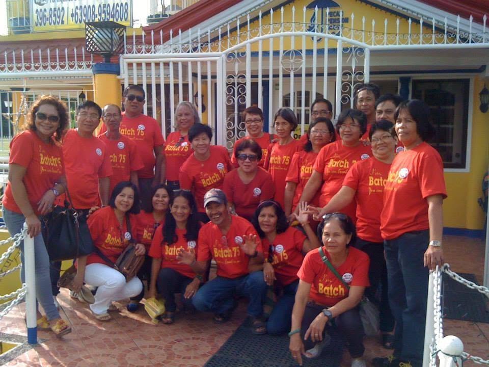 Group of guests in matching shirts gathered at the entrance gate of Pecan Pension House during a community reunion